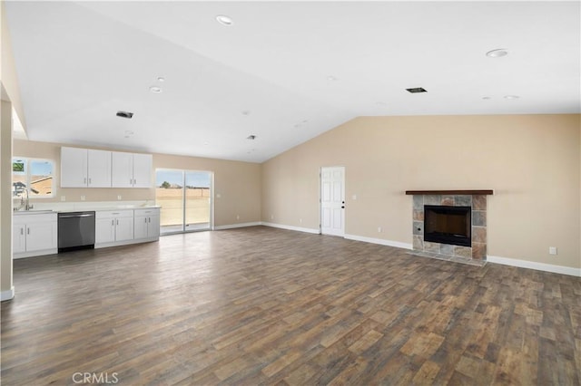 unfurnished living room featuring dark wood finished floors, a sink, vaulted ceiling, a tile fireplace, and baseboards