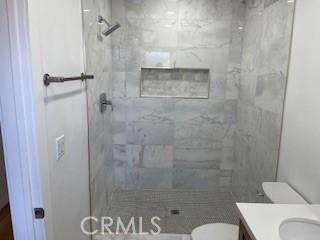 bathroom with tiled shower, vanity, and toilet