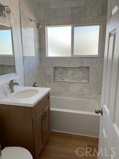 bathroom with washtub / shower combination, vanity, toilet, and wood finished floors