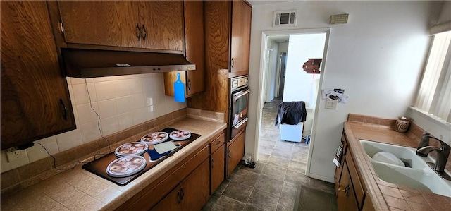 kitchen with brown cabinetry, tile counters, and range hood