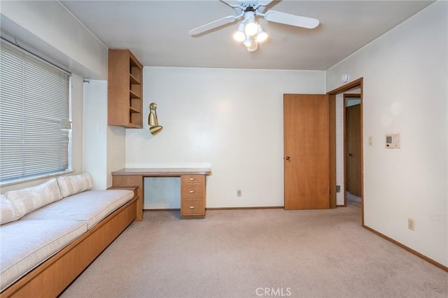 interior space featuring a ceiling fan, light colored carpet, built in desk, and baseboards