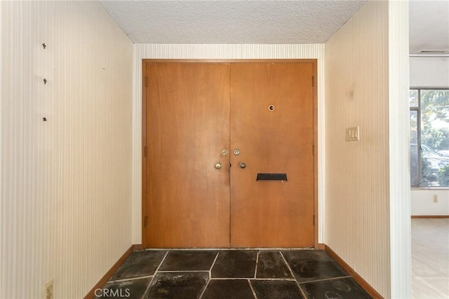 doorway with a textured ceiling and baseboards