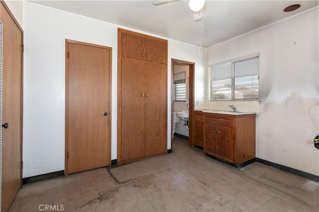 unfurnished bedroom featuring light floors, a ceiling fan, baseboards, and a sink