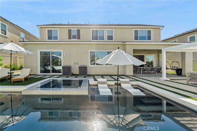 rear view of house with an in ground hot tub, cooling unit, an outdoor pool, and stucco siding