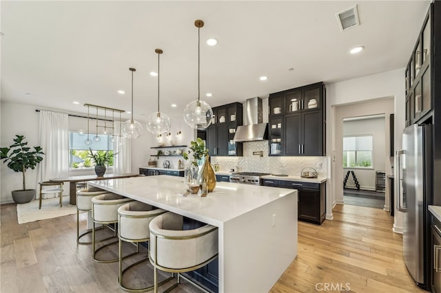 kitchen with decorative backsplash, wall chimney exhaust hood, light wood-type flooring, and freestanding refrigerator