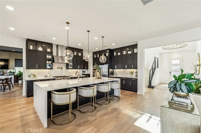 kitchen with light wood-type flooring, wall chimney range hood, light countertops, and freestanding refrigerator