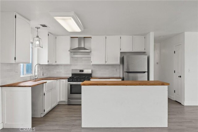 kitchen featuring visible vents, white cabinets, wall chimney exhaust hood, appliances with stainless steel finishes, and wooden counters