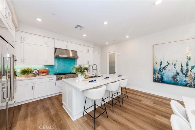 kitchen featuring under cabinet range hood, white cabinetry, visible vents, light wood-type flooring, and decorative backsplash