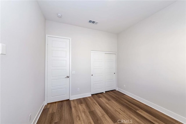 unfurnished bedroom with baseboards, a closet, visible vents, and wood finished floors