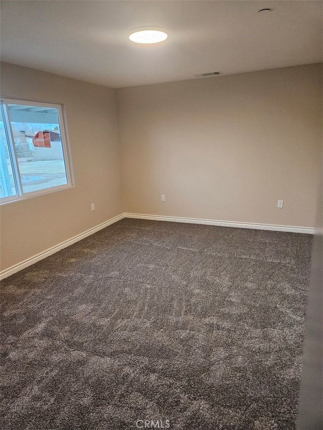 spare room featuring visible vents, dark carpet, and baseboards