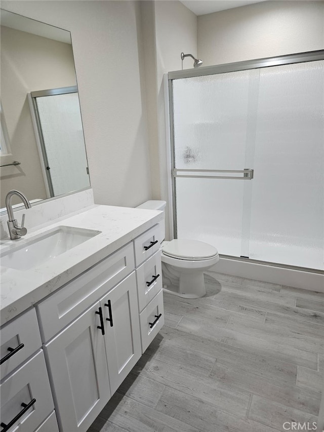 bathroom with toilet, a stall shower, wood finished floors, and vanity