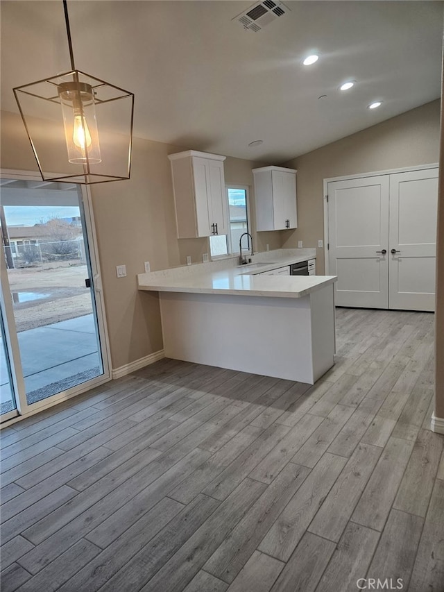 kitchen with a peninsula, a sink, visible vents, white cabinetry, and light countertops