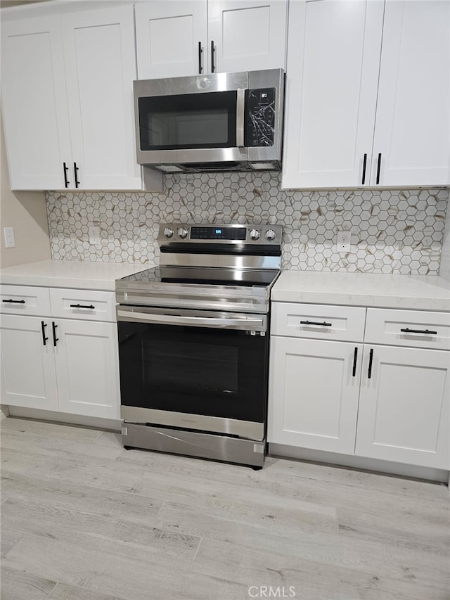 kitchen with light countertops, appliances with stainless steel finishes, light wood-style flooring, and tasteful backsplash