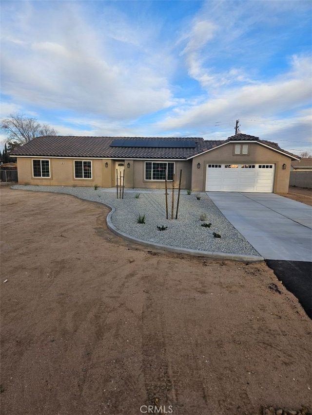 ranch-style home with concrete driveway, stucco siding, an attached garage, and solar panels