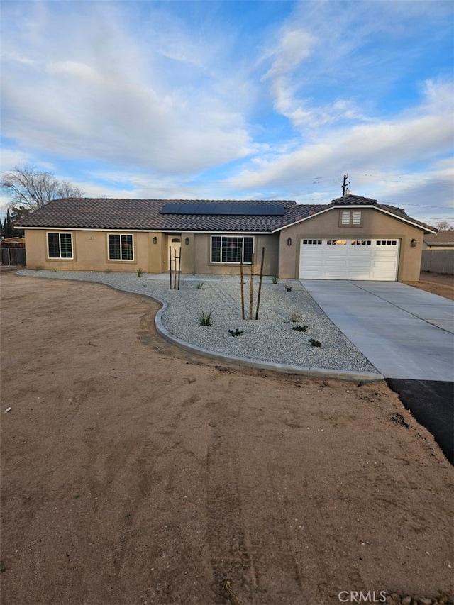 ranch-style house featuring a garage, concrete driveway, stucco siding, and solar panels