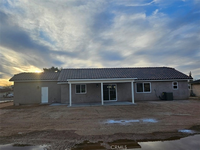 back of property with stucco siding, a patio area, a tiled roof, and central air condition unit