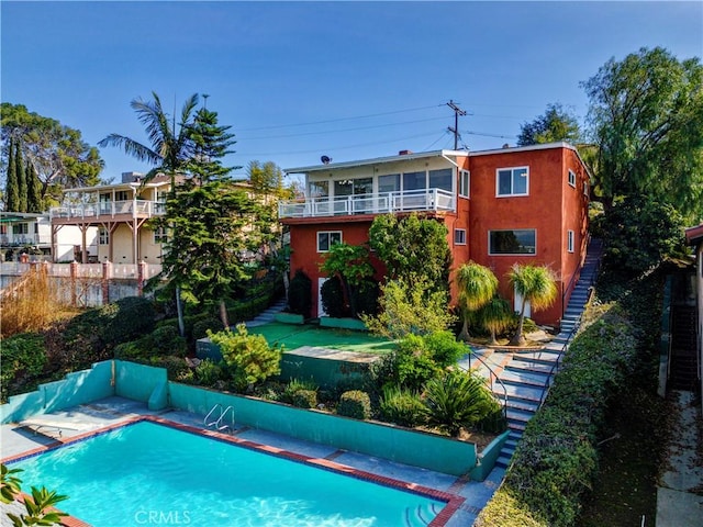 rear view of property with an outdoor pool, a balcony, and stucco siding