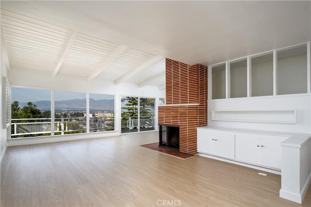 unfurnished living room featuring lofted ceiling with beams, a fireplace, wood finished floors, and a mountain view