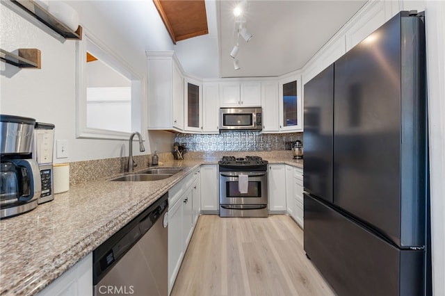 kitchen with stainless steel appliances, a sink, white cabinets, light wood-style floors, and decorative backsplash