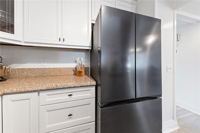 kitchen with white cabinets, glass insert cabinets, wood finished floors, freestanding refrigerator, and light stone countertops