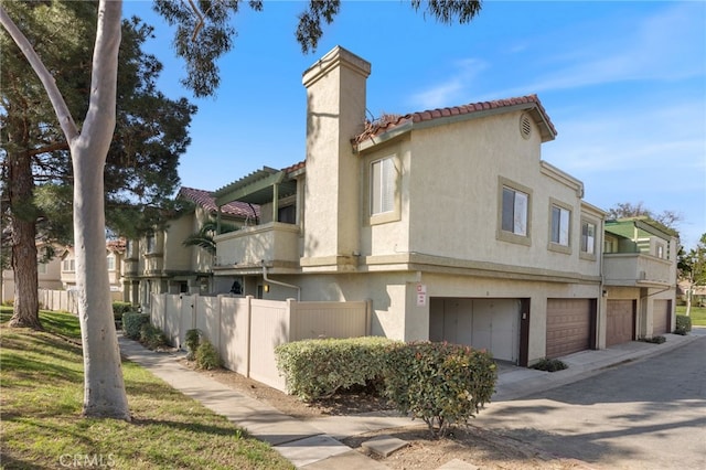 view of property exterior featuring a tile roof, a chimney, stucco siding, an attached garage, and fence