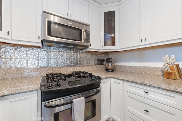 kitchen featuring backsplash, appliances with stainless steel finishes, glass insert cabinets, white cabinetry, and light stone countertops