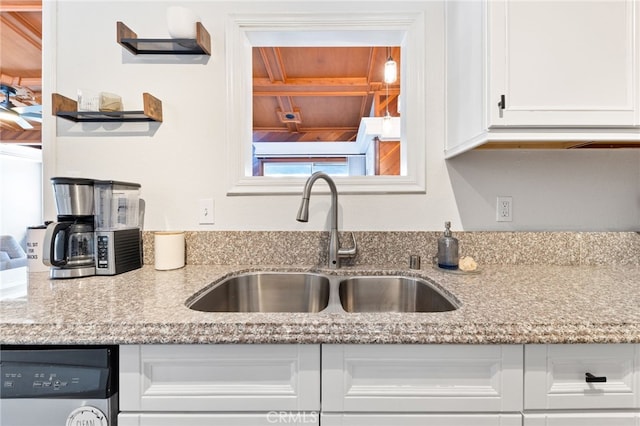 kitchen featuring white cabinetry, a sink, dishwasher, and light stone countertops