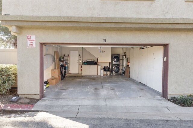 garage featuring water heater and stacked washer / dryer