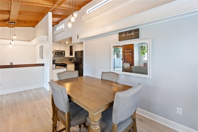 dining area with light wood-type flooring, a high ceiling, baseboards, and beam ceiling