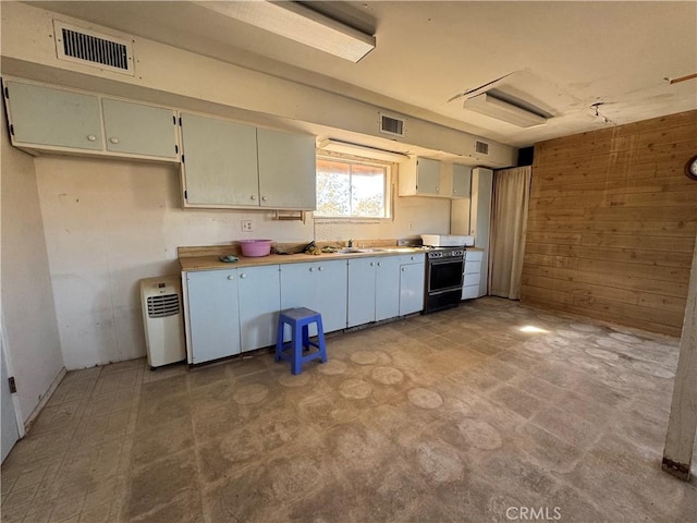 kitchen with wood walls, a sink, visible vents, light floors, and range with gas cooktop