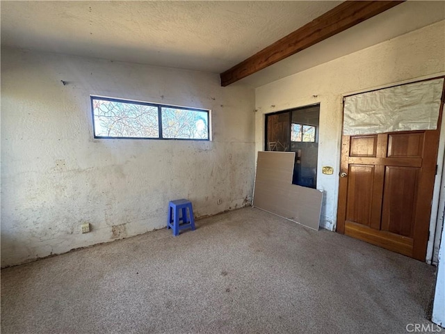 empty room featuring a textured ceiling, beamed ceiling, and carpet flooring