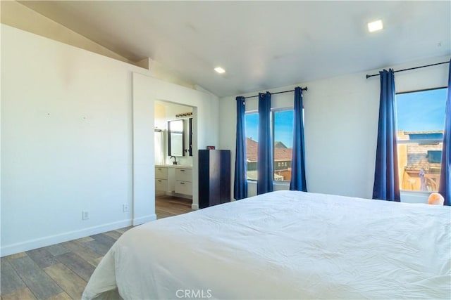 bedroom with baseboards, wood finished floors, ensuite bathroom, vaulted ceiling, and a sink