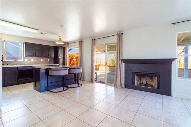 kitchen featuring decorative backsplash, a tiled fireplace, dishwasher, a kitchen breakfast bar, and light countertops