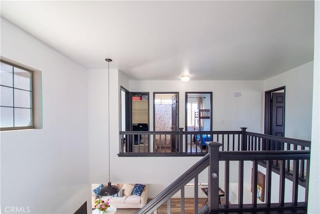 hall with wood finished floors and an upstairs landing