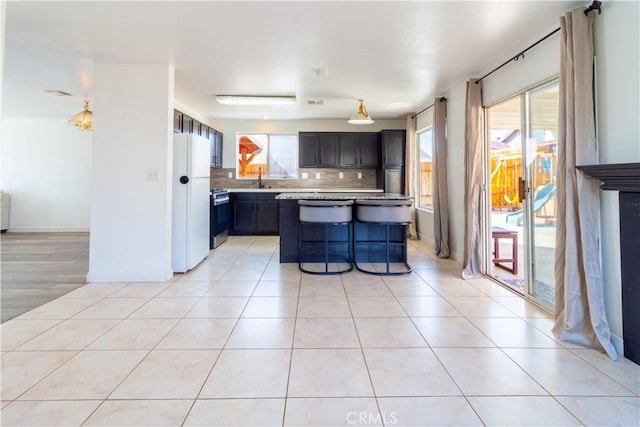 kitchen featuring light tile patterned floors, tasteful backsplash, light countertops, freestanding refrigerator, and stainless steel range with gas stovetop