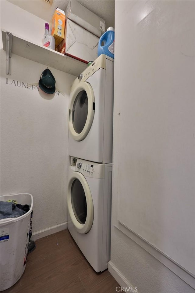 clothes washing area with stacked washer / drying machine, laundry area, baseboards, and wood finished floors