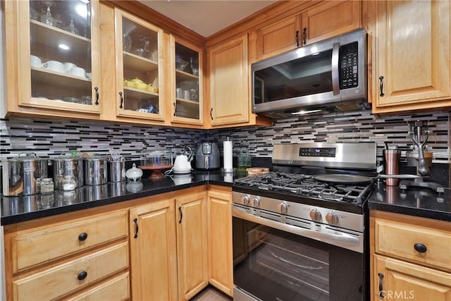 kitchen with appliances with stainless steel finishes, dark stone countertops, backsplash, and glass insert cabinets