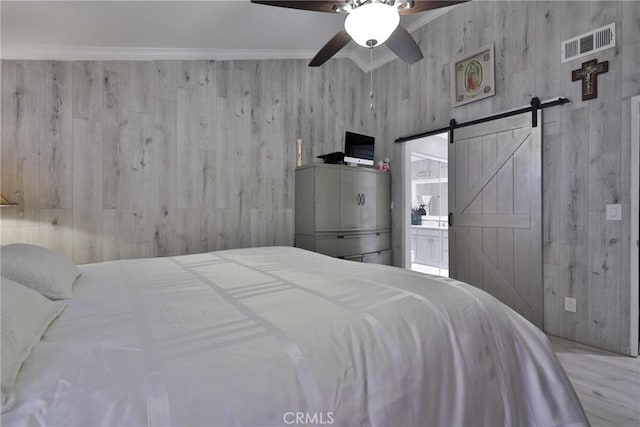 bedroom with a barn door, visible vents, a ceiling fan, ensuite bathroom, and crown molding