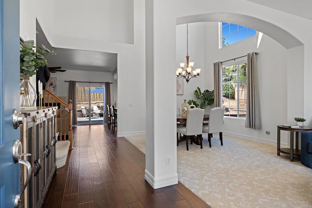 foyer featuring baseboards, a high ceiling, wood finished floors, arched walkways, and a notable chandelier