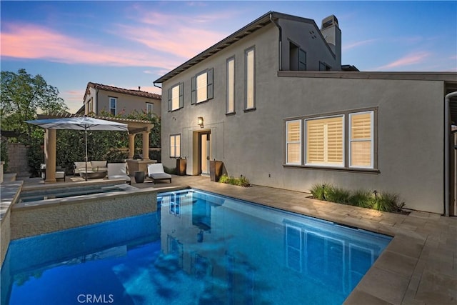 back of house at dusk with an outdoor pool, a chimney, an outdoor hangout area, a patio area, and stucco siding