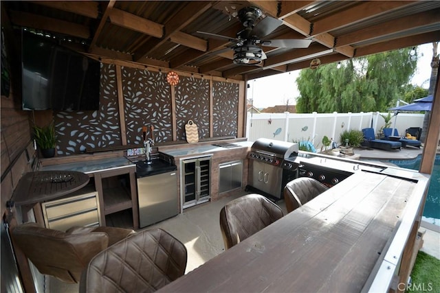 view of patio / terrace featuring wine cooler, a grill, fence, ceiling fan, and exterior kitchen