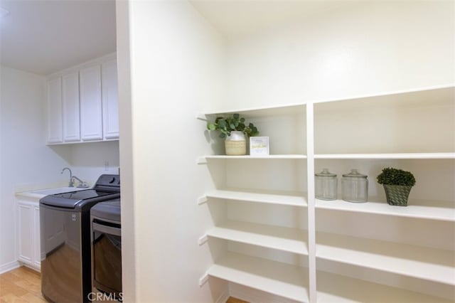 clothes washing area with cabinet space, washer and dryer, light wood-style floors, and a sink