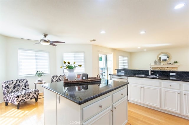 kitchen with light wood-style floors, a center island, white cabinetry, and a sink