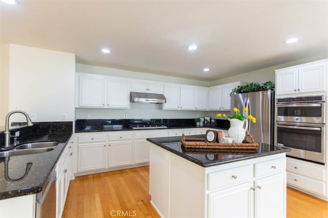 kitchen featuring dark stone countertops, stainless steel appliances, light wood-type flooring, under cabinet range hood, and a sink