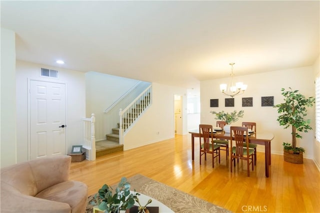 dining space with a notable chandelier, light wood finished floors, visible vents, baseboards, and stairs