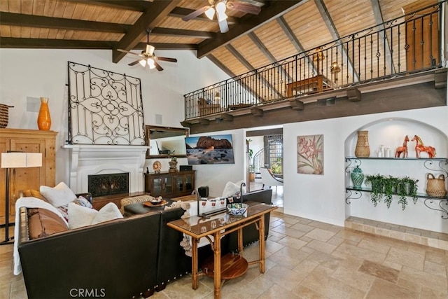 living room featuring a warm lit fireplace, high vaulted ceiling, wooden ceiling, beam ceiling, and stone tile flooring