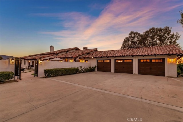 view of front facade with an attached garage, fence, concrete driveway, a tiled roof, and stucco siding