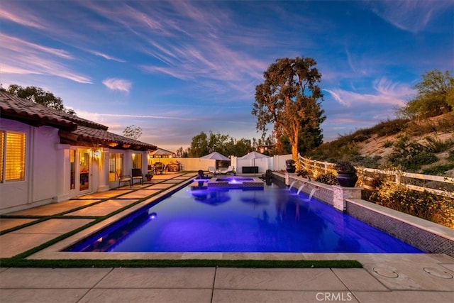 pool at dusk featuring an in ground hot tub, a patio area, a fenced backyard, and a fenced in pool