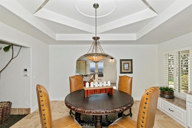 dining room featuring a tray ceiling, arched walkways, and baseboards