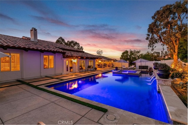 pool at dusk featuring a patio, fence, and a pool with connected hot tub